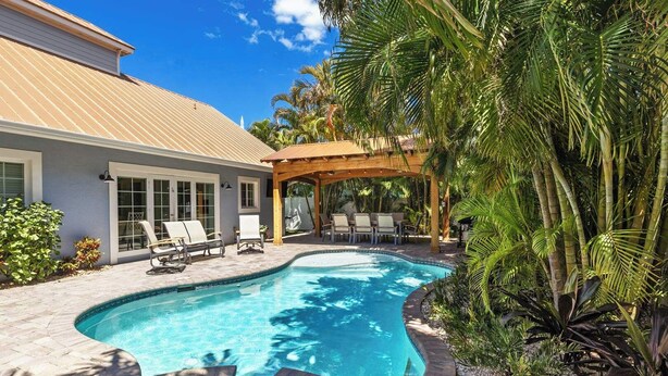 A swimming pool with lounge chairs, a pergola, and tropical plants. - Beach Bound: 1 Block to Beach! Pool & Spa! Perfect AMI location! by Anna Maria Life Vacation Rentals (Holmes Beach)