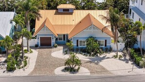 A two-story house with a garage, surrounded by palm trees and a landscaped garden. - Beach Bound: 1 Block to Beach! Pool & Spa! Perfect AMI location! by Anna Maria Life Vacation Rentals (Holmes Beach)