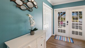 A reception area with teal walls, a white console, a mirror, and a door leading outside.