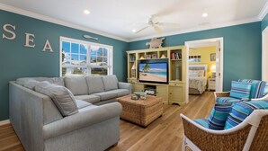 A living room with a grey sofa, a wicker chair, a television, and a bookshelf.