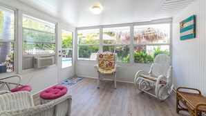 Una habitación soleada con amplias ventanas, muebles de mimbre y un tapete decorativo.