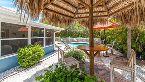 Un área junto a la piscina con una sombrilla de paja, piscina y mobiliario de exterior.