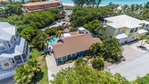 Un barrio residencial con una casa que tiene piscina, rodeado de abundante vegetación y una playa al fondo.
