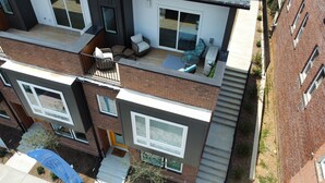 Un edificio residencial de varios pisos con techo plano, ventanas grandes y un balcón con mobiliario exterior.