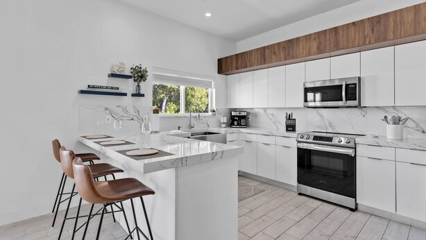 A modern kitchen with white cabinets, a large island with bar stools, a built-in microwave, and a stainless steel oven. - Waterfront, 4Br/3B Home, 5 min from John Pennekamp State Park (Key Largo)
