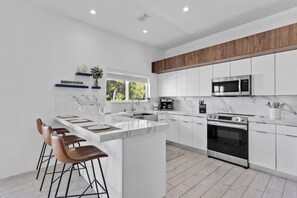 Een moderne keuken met een centraal eiland, barkrukken, een ingebouwde magnetron en een oven.