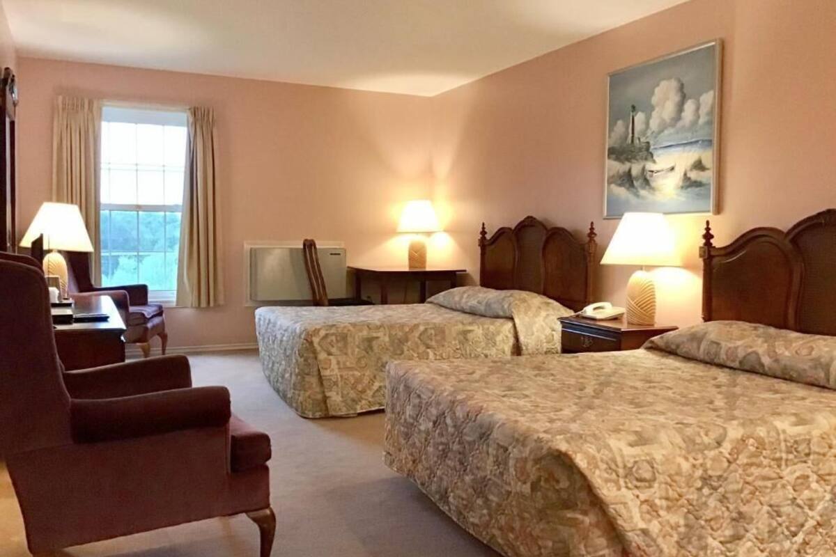 A hotel room with two beds, a chair, a desk, and a painting on the wall.