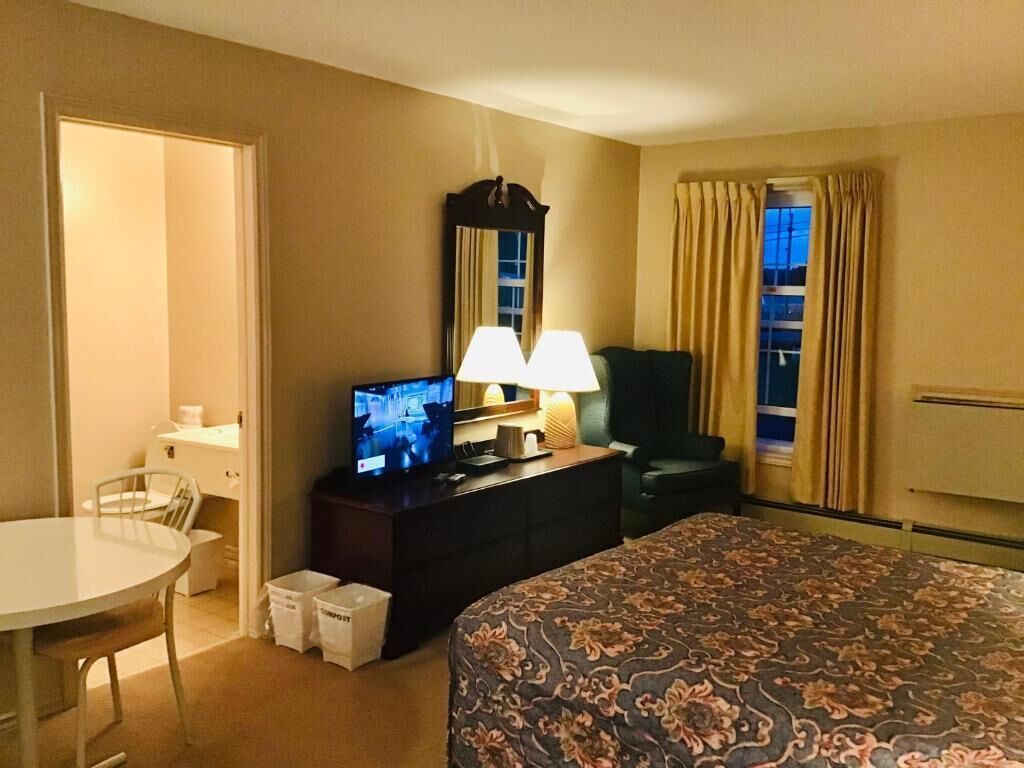 Una habitación de hotel con una cama, un escritorio con televisor, una silla y una lámpara.