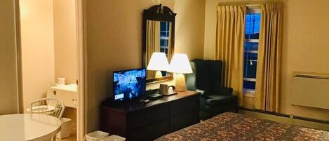 Una habitación de hotel con una cama, un escritorio con televisor, una silla y una lámpara.