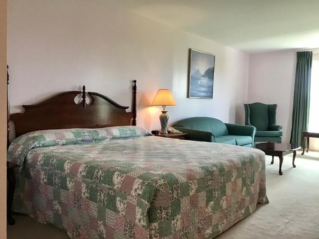 A hotel room with a large bed, a chair, a table, and a lamp.