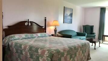 A hotel room with a large bed, a chair, a table, and a lamp.
