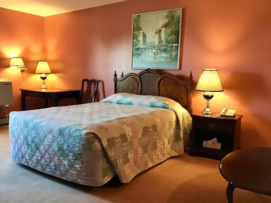Habitación de hotel con una cama grande, dos mesitas de noche con lámparas, una silla y un cuadro en la pared.