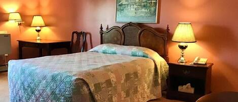 Habitación de hotel con una cama grande, dos mesitas de noche con lámparas, una silla y un cuadro en la pared.