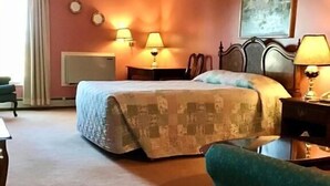 A hotel room with a bed, two bedside lamps, a chair, a desk, and a painting on the wall.