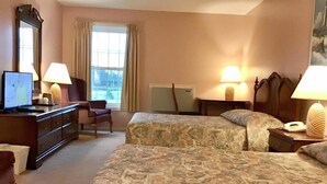 A hotel room with two beds, a desk, a dresser, a chair, and a large window.