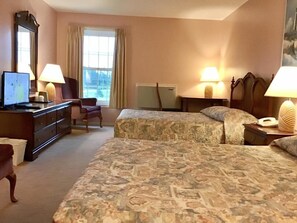 A hotel room with two beds, a desk, a dresser, a chair, and a large window.