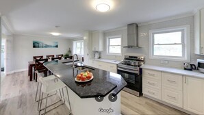 Een moderne keuken met witte kasten, een centraal eiland met een fruitschaal, en een groot raam dat natuurlijk licht binnenlaat.