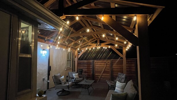 An outdoor patio with wooden beams, string lights, and seating.