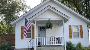 A single-story house with a porch, a number '202' above the entrance, and an American flag on the left side.