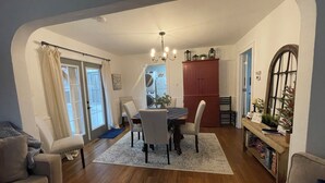 A dining area with a table, chairs, and a chandelier. There is a red cabinet and a window with curtains.