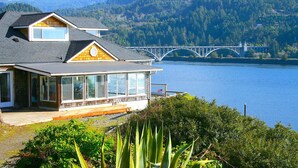 A house with a large bay window overlooking a lake and a bridge. - River’s End-Best Pacific Ocean and Rogue River Views on 2+Acres with a Hot Tub!  (Gold Beach)