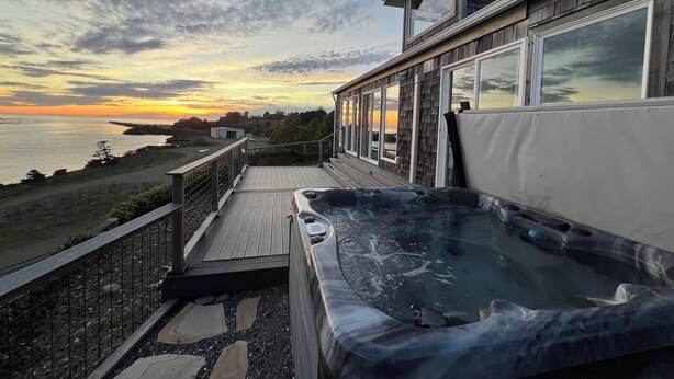A hot tub on a wooden deck with a view of the ocean and a sunset. - River’s End-Best Pacific Ocean and Rogue River Views on 2+Acres with a Hot Tub!  (Gold Beach)