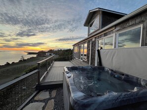 Un bain à remous sur une terrasse en bois, avec vue sur l’océan et sur le coucher du soleil.