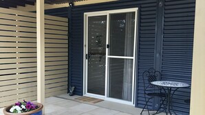 A covered patio area with a sliding glass door, a small table with a metal chair, and two large flower pots.