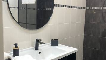 A modern bathroom with a round mirror, a white sink, black cabinets, and a shower area.