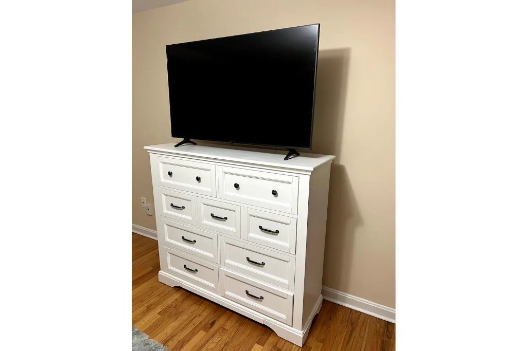 Une commode blanche avec de nombreux tiroirs et un téléviseur à écran plat posé dessus.