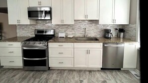 A kitchen with white cabinets, a stainless steel stove, a microwave, a dishwasher, and a tiled backsplash. - Beautifully Renovated, Luxury Home in Beachwood OH (Beachwood)