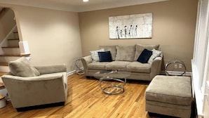 A living room with a beige sofa, a grey armchair, and a round coffee table. There is a staircase in the background and a painting on the wall. - Beautifully Renovated, Luxury Home in Beachwood OH (Beachwood)