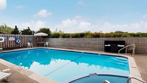 Una piscina con borde de azulejos, una silla de salvavidas y un basurero.