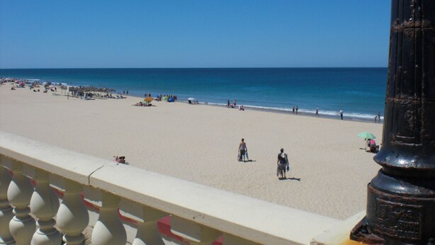 Uma praia com céu claro, areal arenoso e alguns guarda-sóis.