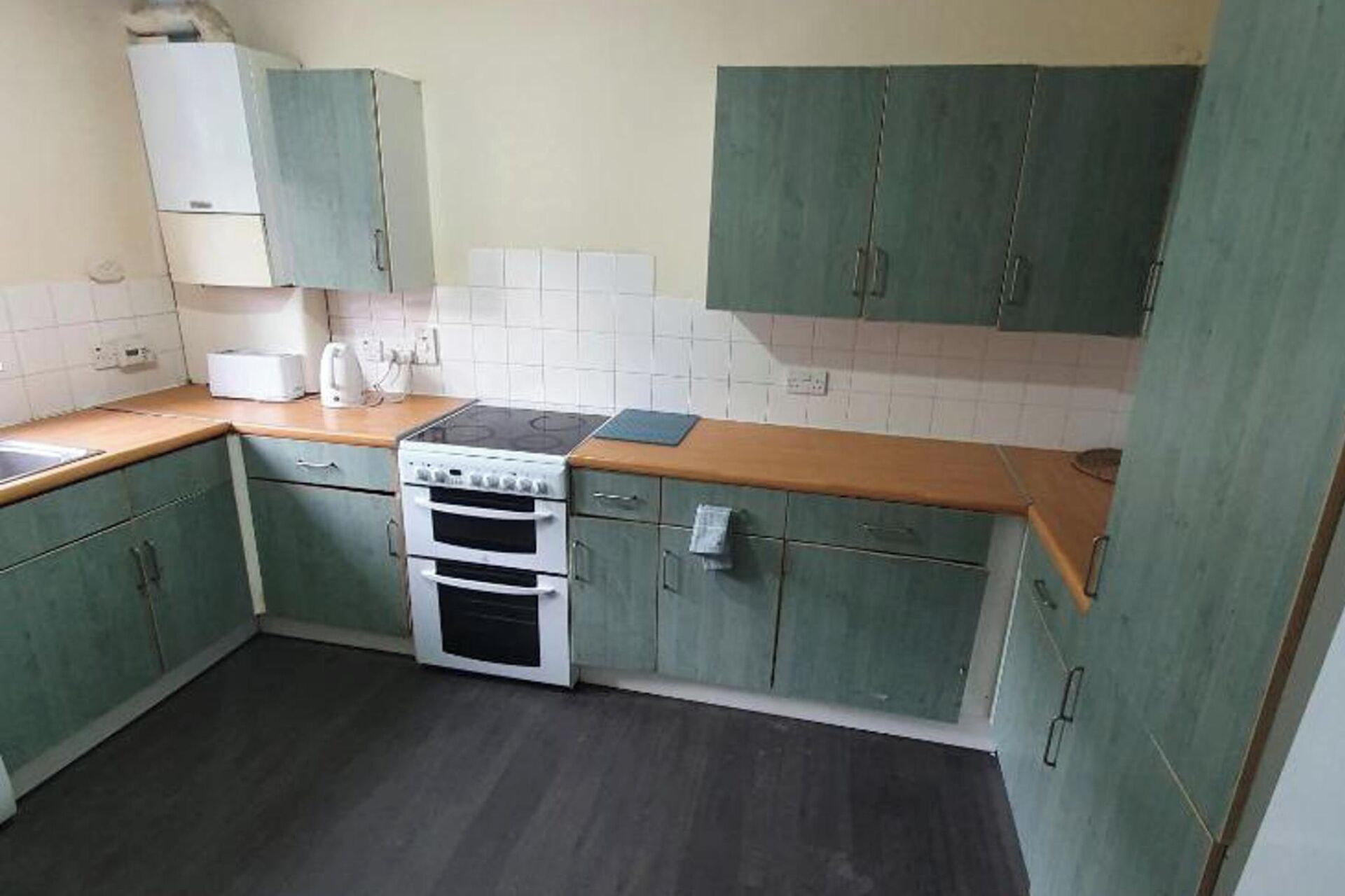 Une cuisine avec des meubles de rangement verts, une cuisinière et un plan de travail.