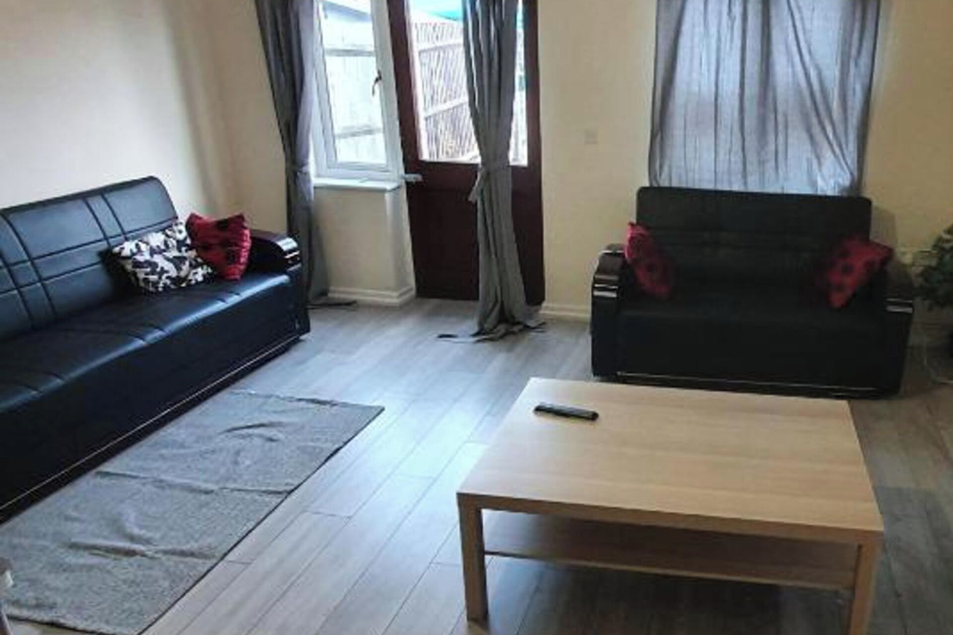 Un salon avec un canapé noir, une table basse en bois et un tapis gris.
