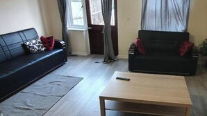 A living room with a black sofa, a wooden coffee table, and a grey rug. - 4 Bed House Sleeps 12 - Private Garden - Parking (London)
