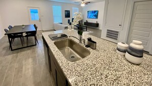 A modern kitchen with a granite countertop, stainless steel sink, and a dining area with a black table and chairs. - 4 BR Cheerful Home Long Term Stay Equipped in Katy (Katy)