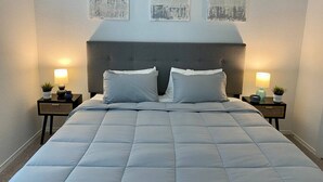 A neatly made bed with a grey headboard, two bedside tables with lamps and small plants, and three abstract wall art pieces above the bed. - 4 BR Cheerful Home Long Term Stay Equipped in Katy (Katy)