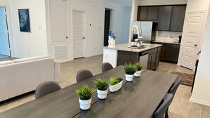 A modern kitchen with dark cabinets, a central island, and a dining area with a long table and chairs. - 4 BR Cheerful Home Long Term Stay Equipped in Katy (Katy)