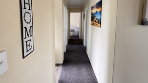 Ein Flur mit einem 'HOME'-Schild an der linken Seite, einem Bett am Ende und einem Landschaftsbild an der Wand.