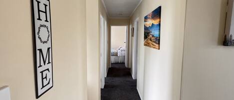 A hallway with a 'HOME' sign on the left, a bed at the end, and a landscape painting on the wall.