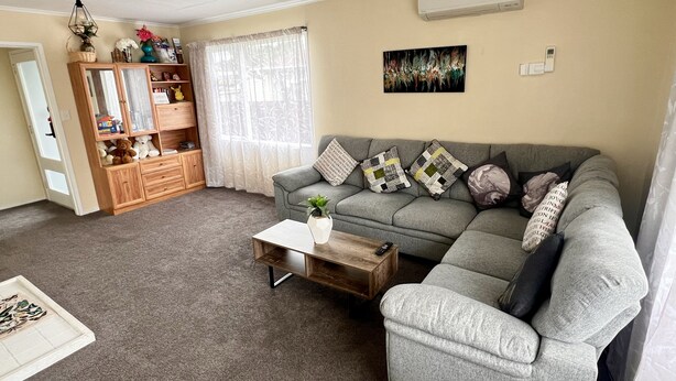 Ein Wohnzimmer mit grauem Sofa, einem Holzschrank, einem Couchtisch und einem Fenster mit durchsichtigen Vorhängen.