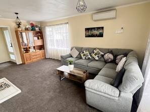 A living room with a grey sofa, a wooden cabinet, a coffee table, and a window with sheer curtains. - Spacious 3 BR Near skyline – 5 Min Walk (Rotorua)