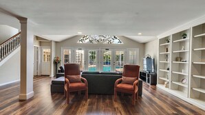 Un salon spacieux doté de parquet, d’une grande fenêtre et offrant une vue sur la piscine.