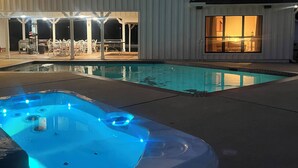 Une piscine avec un jacuzzi, un patio couvert et un bâtiment doté de nombreuses fenêtres.