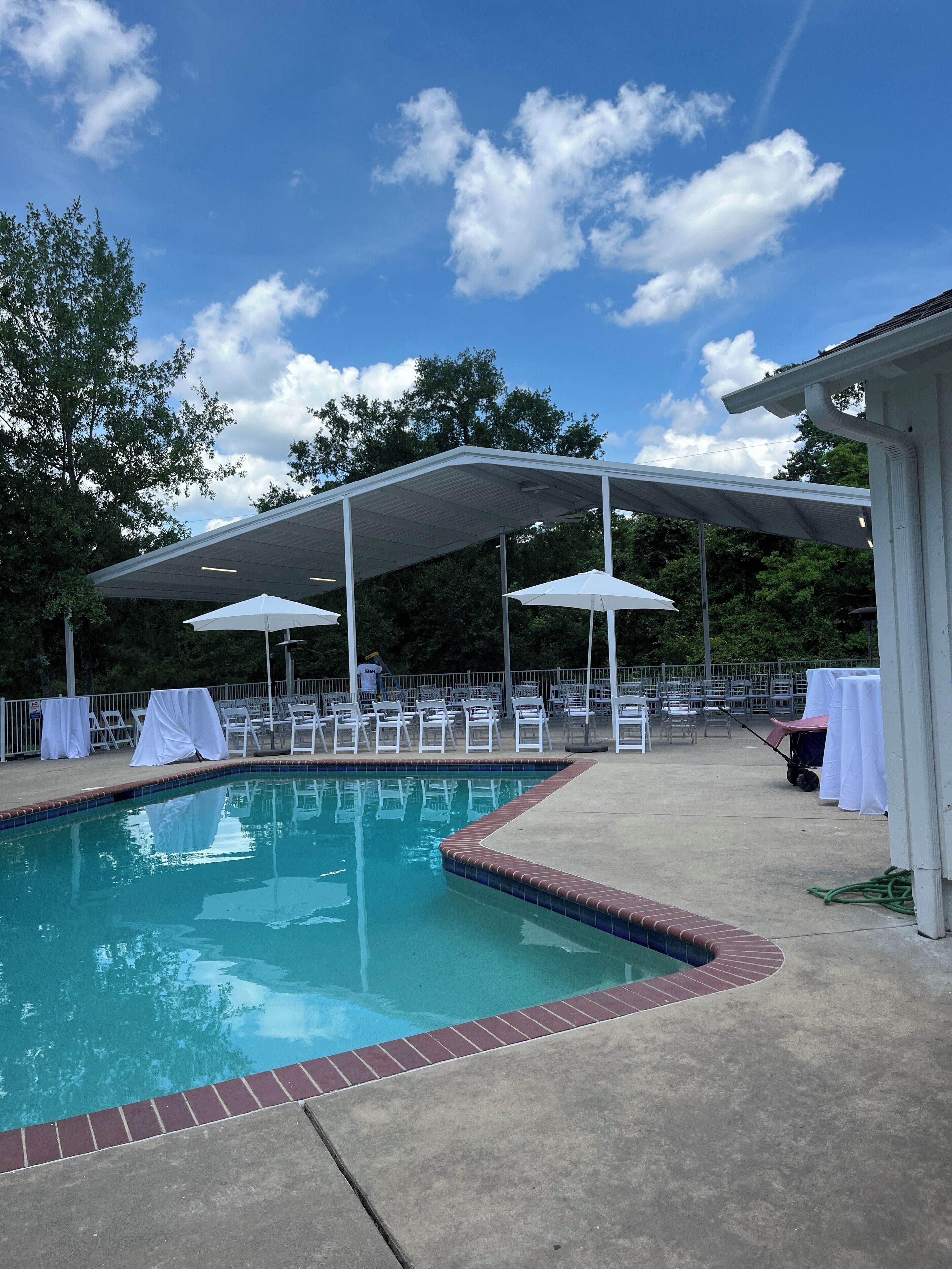 A swimming pool with a covered seating area and chairs.