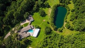 Vue aérienne d’une propriété dotée d’une piscine, d’une grande pelouse et entourée d’une forêt dense.