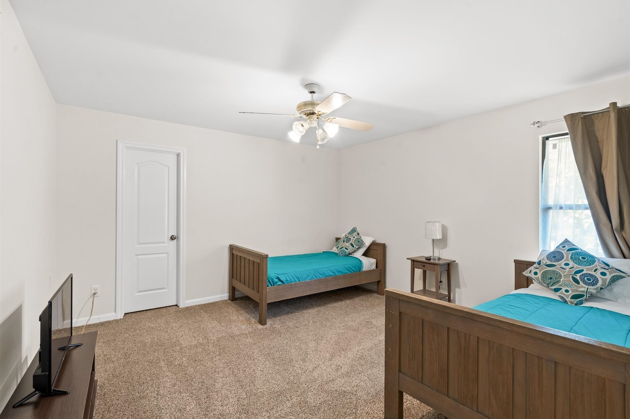 A bedroom with two single beds, a ceiling fan, a TV, and a window with curtains.