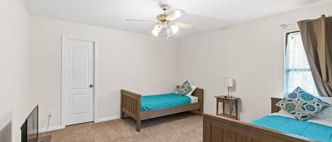 A bedroom with two single beds, a ceiling fan, a TV, and a window with curtains.